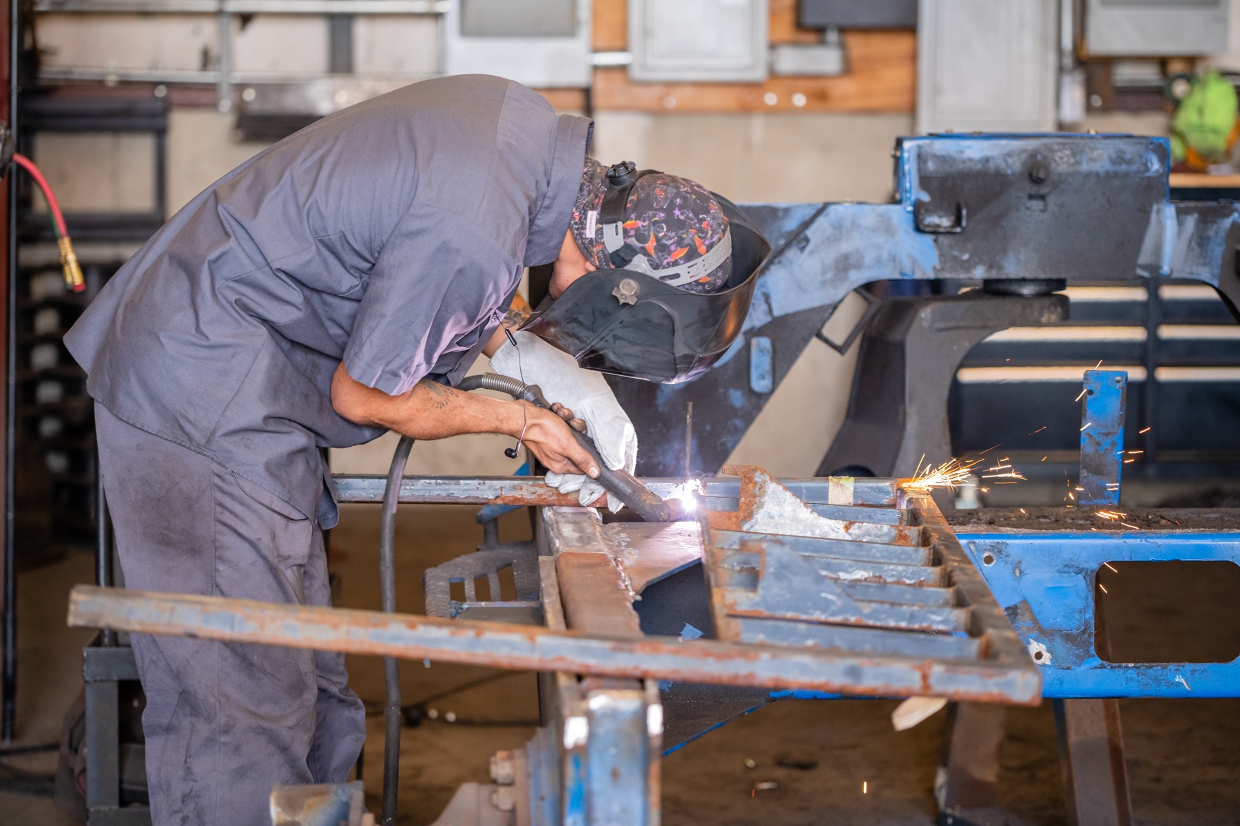 man custom welding metal in a workshop with protective gear on